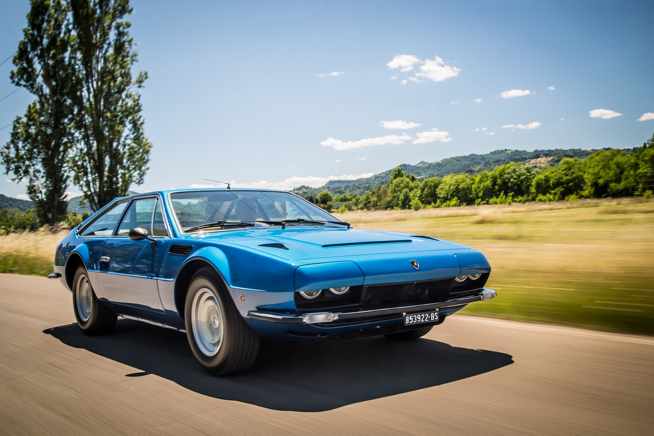 Cinque decadi fa vedeva la luce la Lamborghini Jarama GT, ultima evoluzione del concetto di berlinetta granturismo 2+2 con motore 12 cilindri in posizione anteriore. Presentata al Salone di Ginevra 1970, la Jarama venne chiamata così in omaggio a un famosa zona a nord di Madrid a sua volta nota per l’allevamento dei tori da corrida. Basata tecnicamente sulle precedenti 400 GT e Islero, venne curata stilisticamente dal grande Marcello Gandini e il risultato è sotto gli occhi di tutti. Pur arrivando al principio degli anni ‘70, si notano subito le linee tese e angolari che sarebbe poi diventate un simbolo di quel decennio e che la sapiente matita dello stilista italiano seppe interpretare alla perfezione. Tecnicamente, la ciclistica viene rinnovata, con un impianto frenante a 4 dischi (anteriori autoventilati) di grandi dimensioni, la carreggiata allargata di 10 centimetri, adesso a 1490 mm, e i cerchi in magnesio Campagnolo da 15”. Il motore, alimentato da 6 carburatori doppio corpo Weber 40 DCOE, è il collaudato V12 di Sant’Agata, con doppio albero a camme in testa per ogni bancata, capace di 350 CV per una velocità massima di 260 Km/h. Una parte degli esemplari venne assemblata presso gli stabilimenti della Carrozzeria Marazzi vicino a Varese, là dove prima sorgeva la Islero, un’altra direttamente nella sede della Carrozzeria Bertone a Grugliasco, in provincia di Torino. Gli ultimi 100 esemplari di Jarama prodotti, 1972, saranno un “ibrido”, con i pannelli carrozzeria stampati da Bertone e l’assemblaggio presso la Marazzi. Gli interni sono lussuosissimi, con rivestimento in pelle ed aria condizionata, e un’abitabilità di tutto rispetto per una vettura sportiva, capace anche di offrire un bagagliaio degno di questo nome. Nel 1972 arriva la Jarama GTS: potenza aumentata a 365 CV, una nuova presa d’aria e una nuova plancia in abitacolo. Diversi, sulla “GTS” anche i cerchi in lega, meno elaborati e senza il dado singolo centrale. La Jarama GT e poi GTS si è ritagliata uno spazio nella storia della Casa. Viene ricordata, come detto, come una delle prime vetture a proporre quei canoni che sarebbero poi diventati un riferimento in quegli anni ma anche perchè è stata l’ultima granturismo con motore anteriore proposto dalla Casa di Sant’Agata Bolognese. Da lì in poi, eccezion fatta per i Super SUV LM 002 e Urus, le Lamborghini avranno solo il motore posteriore. Unità prodotte di Lamborghini Jarama GT Lamborghini Jarama GT: 1970-1973, 176 Lamborghini Jarama GTS: 1972-1976, 152